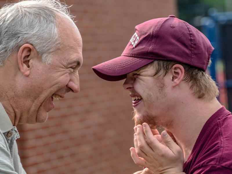 Parent and child smiling at each other face to face; background is a brick wall