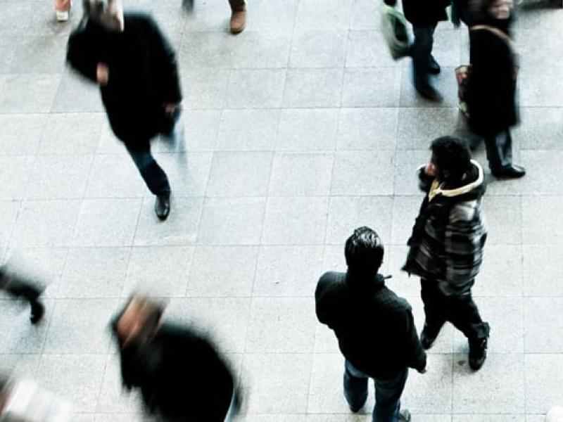 People walking on a white / grey sidewalk dressed in winter clothes. photo taken from about 20-30 feet above them