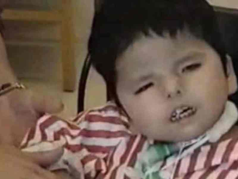 Young toddler with striped shirt on looking at the camera while an adult helps them