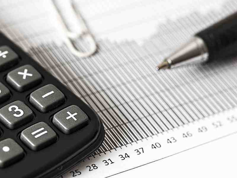 close up image of a graph, a pen, paper clip and caclulator on a white desk