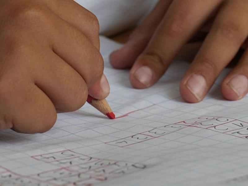 Close up of a youth's hands doing work on a piece of graph paper