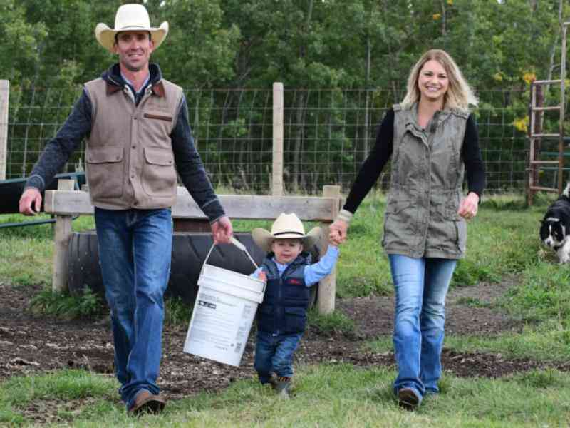 Photo of two farmers with their child carrying a bucket on their farmland