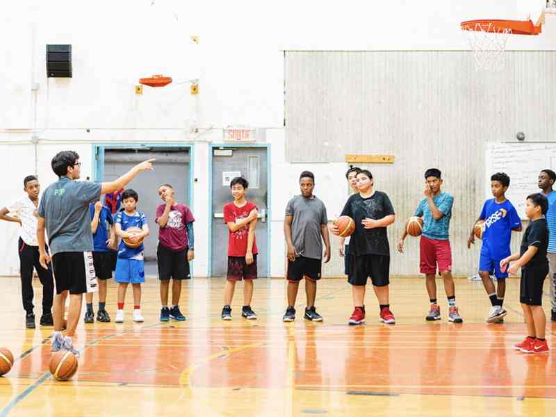 Group of youth in a basketball gym. Two coaches speaking to the group