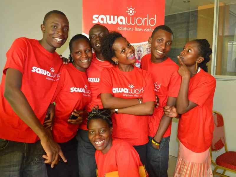 Group of youth from Uganda wearing red Sawa World t shirts smiling at the camera