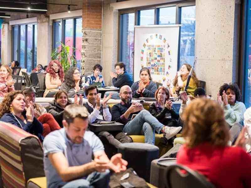 People seated in small groups in a large group at Dynamo's Hackathon