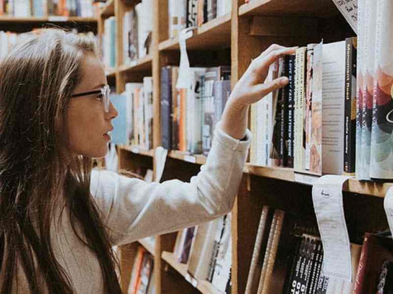 Photo of a young teen picking out a book in a bookstore or library