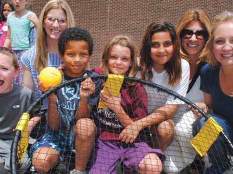 Photo of adults and elementary school aged kids playing spikeball at recess