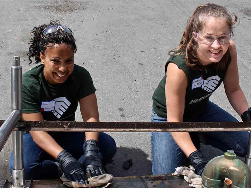 Two people with work gloves on building a metal structure