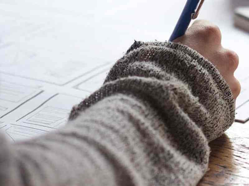 Photo of student's hand writing in a notebook on a desk