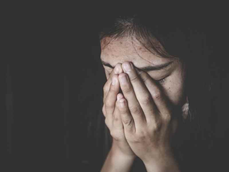 Woman with closed eyes and hands over her face; dark background