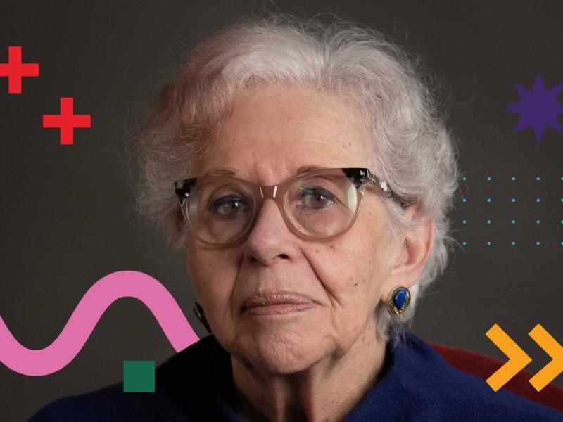 Portrait of Marta Gil, a person with short gray hair and round glasses, wearing blue clothing and a blue-stone earring, against a dark background with colorful graphic shapes (red crosses, purple star, dotted pattern, pink wave, and yellow arrows).