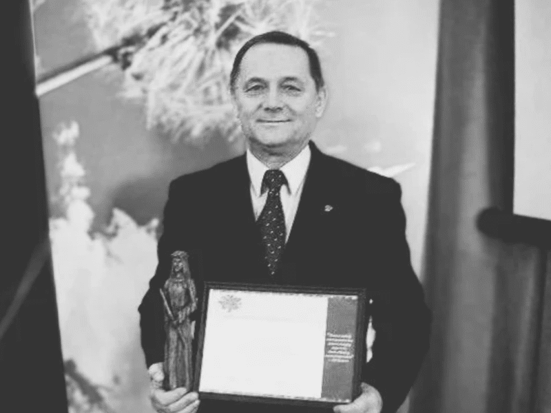 a black and white photo of a man in a suit holding diploma and statuette