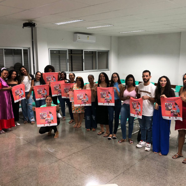 Vê-se uma foto de diversas pessoas com cartazes em cor rosa