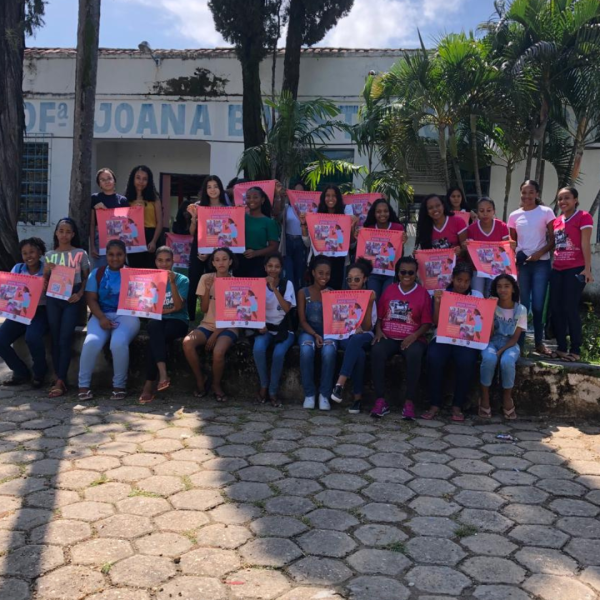Vê-se uma foto de diversos estudantes sentados com cartazes em cor rosa
