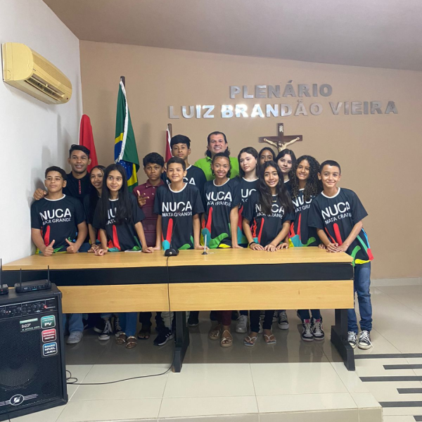 Vê-se uma foto de diversos estudantes com o Vereador Rodolfo Izodoro (Homem branco de cabelos longos e pretos) atrás de uma mesa com o escrito na parede atrás deles "Plenário Luiz Brandão Vieira"