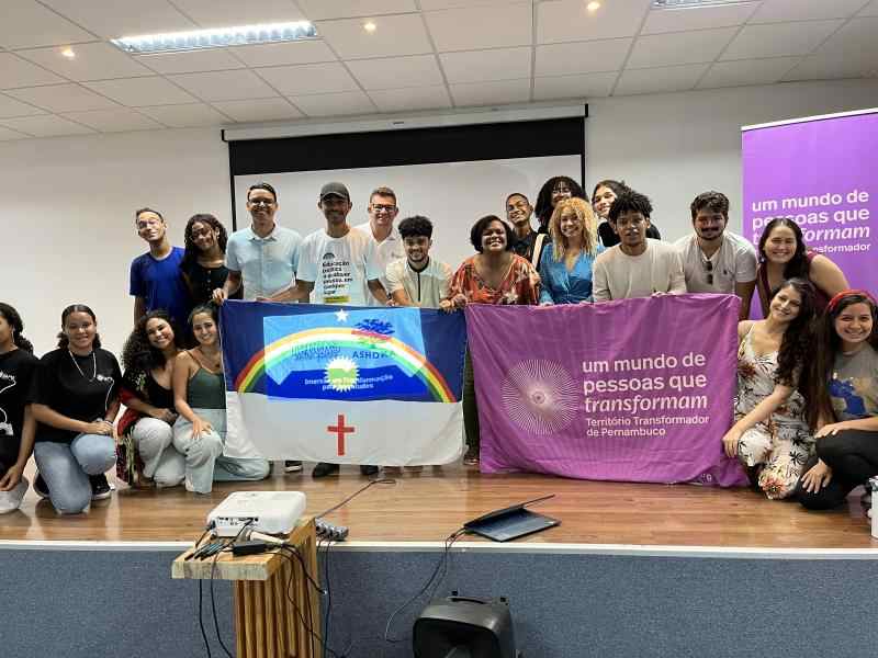 Diversas pessoas sorrindo em cima de um palco segurando as bandeiras do Pernambuco e do Território Transformador do Pernambuco