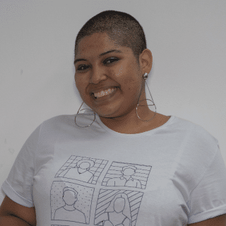 Beatriz is a black girl with shaved hair. She is wearing a white T-shirt