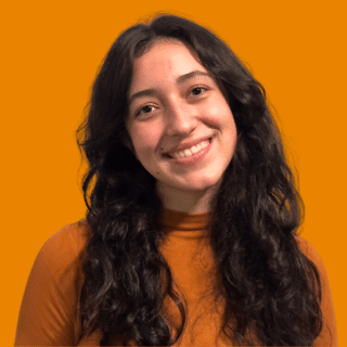 Érica é uma jovem branca de cabelo castanho, comprido e ondulado. Ela sorri para a foto
