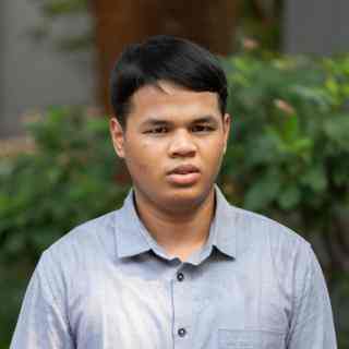 Headshot of AYC Ade wearing a grey shirt on a nature background.