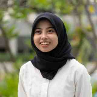 Headshot of AYC Adinda smiling at the camera wearing a black hijab and white shirt on a nature background.