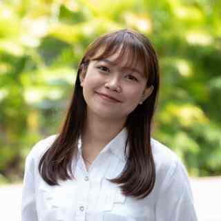 Headshot of AYC Alya smiling directly at the camera wearing a white shirt on a nature background.