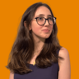 Gabriela é uma jovem branca com cabelos médios castanhos. Ela usa óculos e olha para o lado