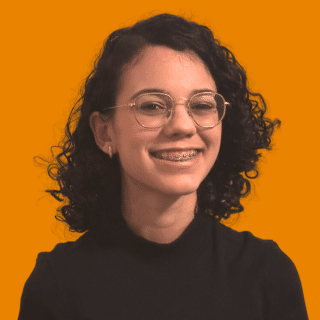 Heloíse é uma jovem branca de cabelo curto, escuro e enrolado. Ela sorri para a foto e usa óculos