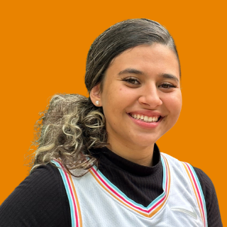 Isabela é uma jovem de cabelos loiros e cacheados. Ela usa um rabo de cavalo baixo e sorri para a foto