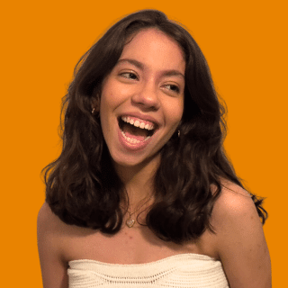 Júlia é uma jovem branca com cabelo escuro, na altura dos ombros. Ela olha para o lado com um sorriso largo.