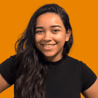 Maria Eduarda é uma jovem de cabelos longos, escuros e ondulados. Ela veste uma blusa preta e sorri para a foto