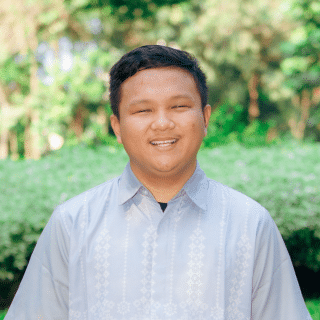 Headshot of a boy smiling at the camera on a nature background.