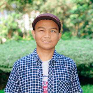 Headshot of a boy smiling at the camera on a nature background.