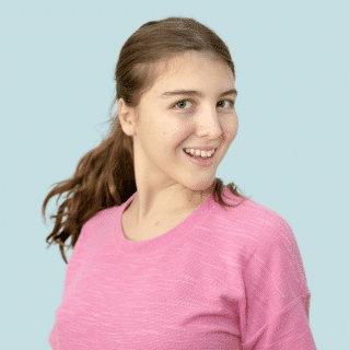 Giovana é uma jovem branca de cabelo castanho claro preso em um rabo de cavalo. Ela sorri e veste uma blusa rosa