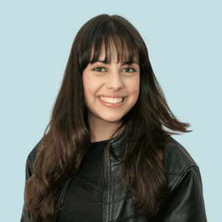 Melyssa é uma jovem branca de cabelos castanhos lisos, longos e com franja. Ela usa uma jaqueta de couro preta e uma blusa preta e sorri para a foto