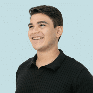 Rafael é um jovem pardo de cabelo curto e castanho. Ele veste uma camisa polo preta e sorri