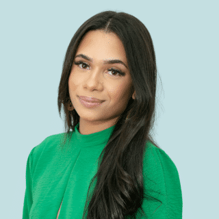 Yasmin é uma jovem parda de cabelo castanho, longo e liso. Ela veste uma blusa verde e sorri levemente para a foto